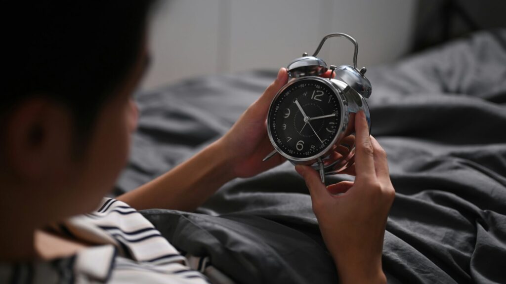 ベッドで目覚まし時計を手に持っている男性