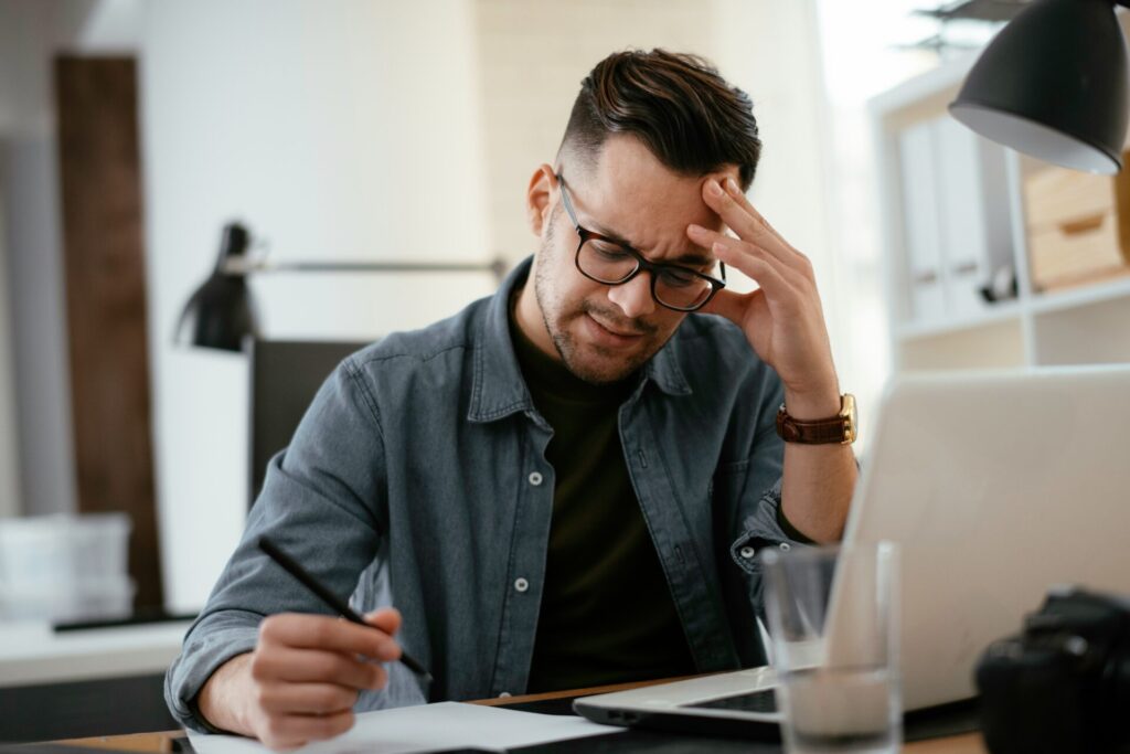 頭を抱えながらパソコン作業をしている男性